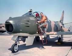 a man sitting in the cockpit of an airplane with another person standing next to it