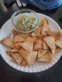 a white plate topped with tortilla chips next to a bowl of dip on top of it