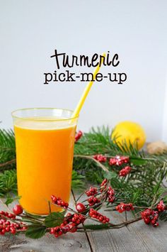 a glass filled with orange juice sitting on top of a table next to pine branches