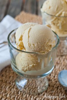 three scoops of vanilla ice cream in a glass bowl on a table with spoons