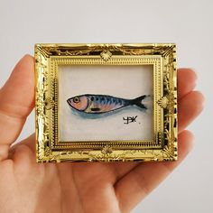 a painting of a fish is displayed in a gold frame with an embellishment