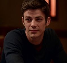 a young man sitting at a table with his hand on his chin and looking into the camera