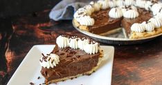 a slice of chocolate pie with whipped cream on top sitting on a plate next to another pie