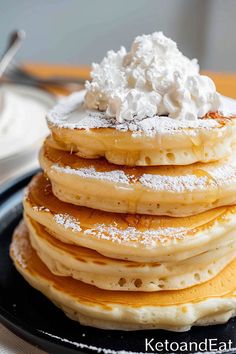 a stack of pancakes covered in powdered sugar and whipped cream on a black plate