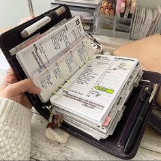 a person is holding a wallet full of papers and pens in front of a pile of books