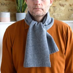 a man wearing an orange sweater with a gray scarf around his neck and a cactus in the background