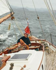 a man sitting on the deck of a sailboat in the ocean next to another boat