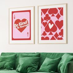 two posters on the wall above a green couch in a white room with pink and red decor