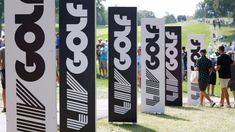 several black and white signs are lined up on the grass with people in the background