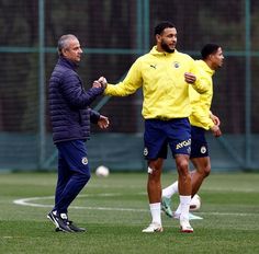 two men in yellow and blue jackets on a soccer field with one man holding his hand out