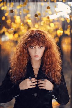 a woman with long red hair standing in front of a forest filled with golden lights