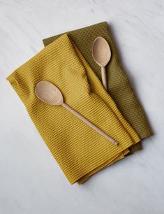 two wooden spoons sitting on top of yellow napkins with matching green and brown cloth