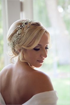 a woman in a white dress is looking down at her wedding hairpiece with flowers on it