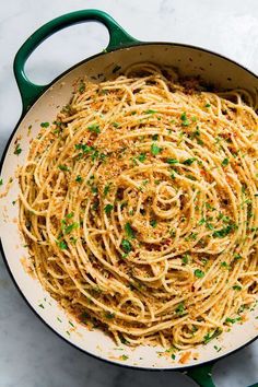 pasta with parmesan cheese and herbs in a green skillet on a marble surface