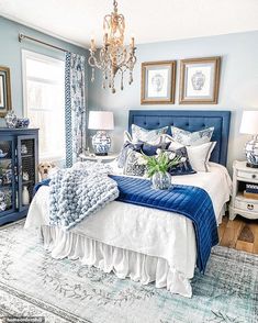 a blue and white bedroom with chandelier, bed, pillows, rugs and pictures on the wall