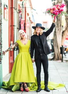 a man and woman holding hands while standing next to each other on the sidewalk in front of a building