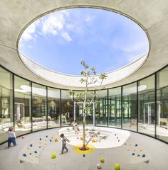 children playing in an indoor play area with glass walls and round ceiling, surrounded by colorful balls