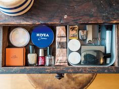 an open drawer filled with various items on top of a wooden table next to a hat