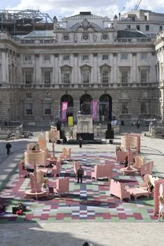 people are sitting on the ground in front of a large building with pink and green squares