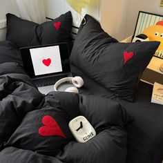 a bed with black comforter and red hearts on it, next to a laptop