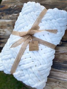 a white blanket wrapped in twine and tied with a brown ribbon, sitting on top of a wooden bench