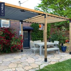 an outdoor patio with a table and chairs under a pergolated roof next to a brick building