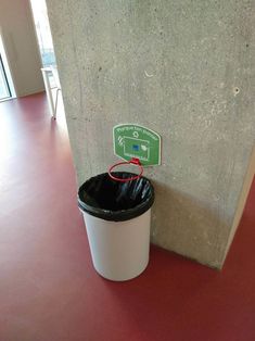 a trash can sitting next to a wall with a sign on it