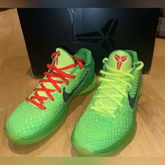 a pair of green and red shoes sitting on top of a wooden floor next to a box