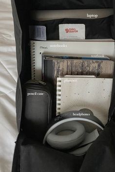 the contents of a bag are neatly packed on top of a bed, including headphones and notebooks