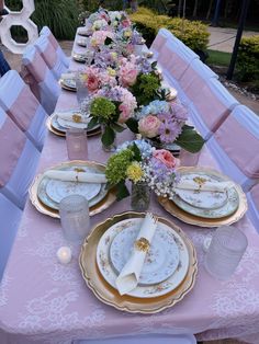 the table is set with pink and white plates, silverware, and floral centerpieces