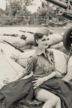 an old photo of a woman in uniform sitting on the ground next to some tanks