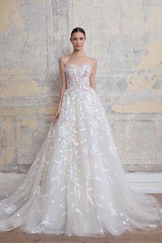 a woman standing in front of a wall wearing a dress with white flowers on it