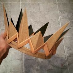 a person holding up a cardboard crown made out of pieces of paper on the floor