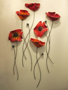 four red flowers on a white wall with long stems in the shape of wavy lines