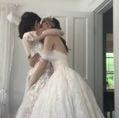 two brides hugging each other in front of a mirror at the same time as they are dressed for their wedding day