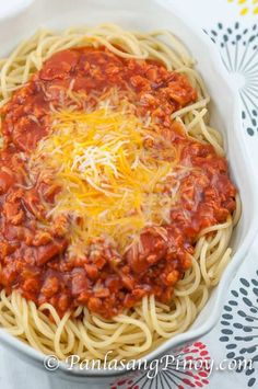 a white bowl filled with spaghetti and sauce on top of a tablecloth covered table