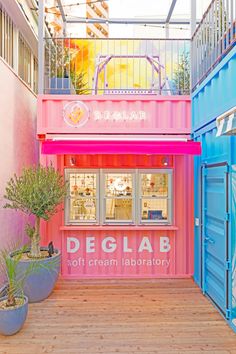 a pink and blue store front with potted plants in the foreground, on wooden flooring