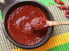 a wooden spoon full of chili sauce on top of a colorful table cloth with peppers in the background