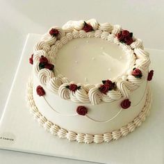 a white cake sitting on top of a table covered in frosting and red roses