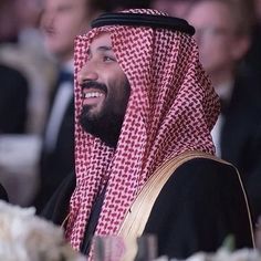 a man with a beard wearing a red and white checkered headdress sitting in front of other people