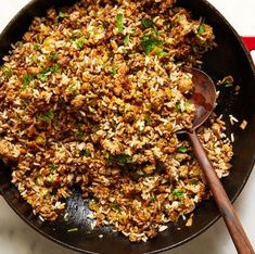 a skillet filled with rice and meat on top of a table next to a wooden spoon