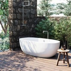 a large white bath tub sitting on top of a wooden floor next to a stone wall