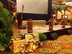 a stage set up for an event with palm trees and other decorations on the floor