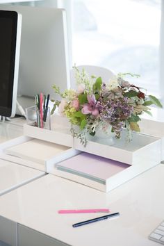 a desk with a computer, keyboard and flowers on it