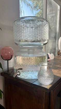 two glass vases sitting on top of a wooden table next to a potted plant