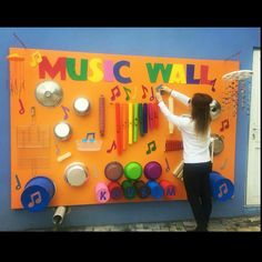 a woman standing in front of a music wall with musical instruments on it's side