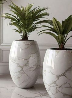 two white vases with plants in them sitting on a marble countertop next to each other