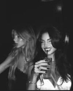 two beautiful women standing next to each other holding drinks