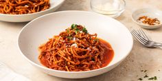 two bowls filled with spaghetti and sauce on top of a marble counter next to silverware