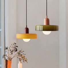 three different colored lights hanging from the ceiling above a table with flowers in vases